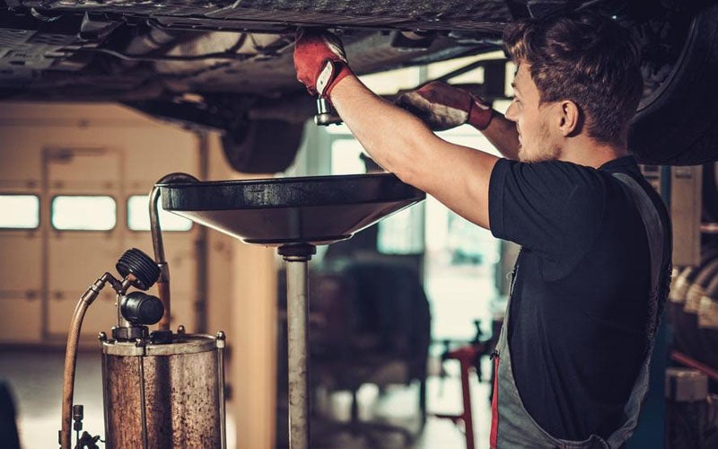 mechanic draining oil from a vehicle on a lift